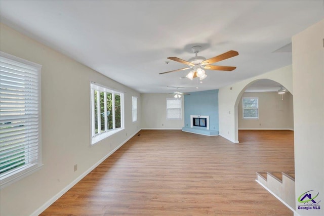 unfurnished living room featuring arched walkways, light wood-style flooring, a ceiling fan, and plenty of natural light