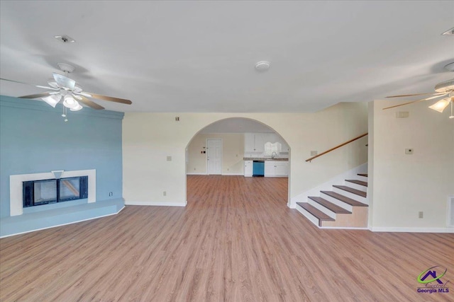 unfurnished living room featuring wood finished floors, arched walkways, ceiling fan, and a glass covered fireplace