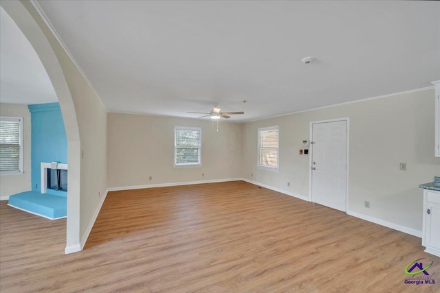 unfurnished living room with crown molding, baseboards, light wood finished floors, and ceiling fan