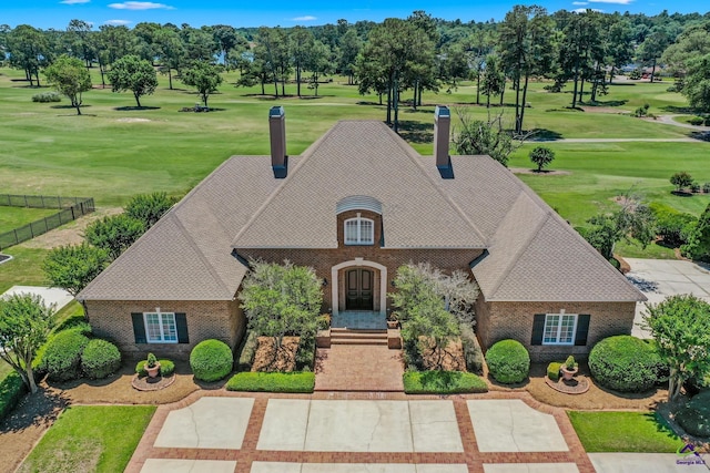 french country home featuring brick siding, a front yard, a shingled roof, and a chimney
