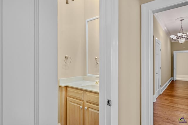 bathroom featuring a notable chandelier, crown molding, vanity, wood finished floors, and baseboards