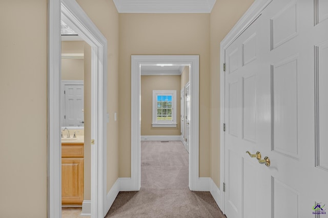 hallway featuring ornamental molding, a sink, light carpet, and baseboards