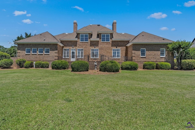 rear view of property with brick siding, a lawn, and a chimney
