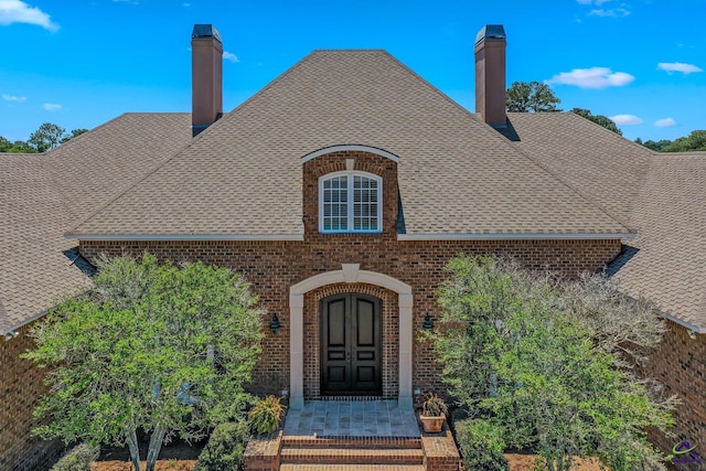 exterior space featuring brick siding, roof with shingles, and a chimney