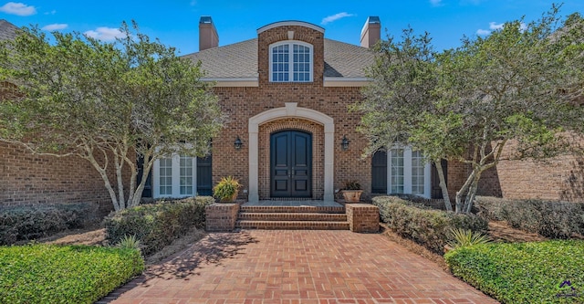 view of exterior entry with a chimney and brick siding