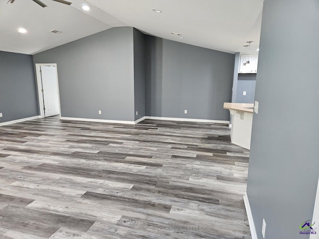 unfurnished living room with recessed lighting, baseboards, vaulted ceiling, and wood finished floors