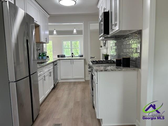 kitchen with backsplash, white cabinetry, light stone countertops, appliances with stainless steel finishes, and light wood-style floors