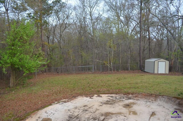 view of yard featuring a shed, a fenced backyard, a forest view, and an outbuilding