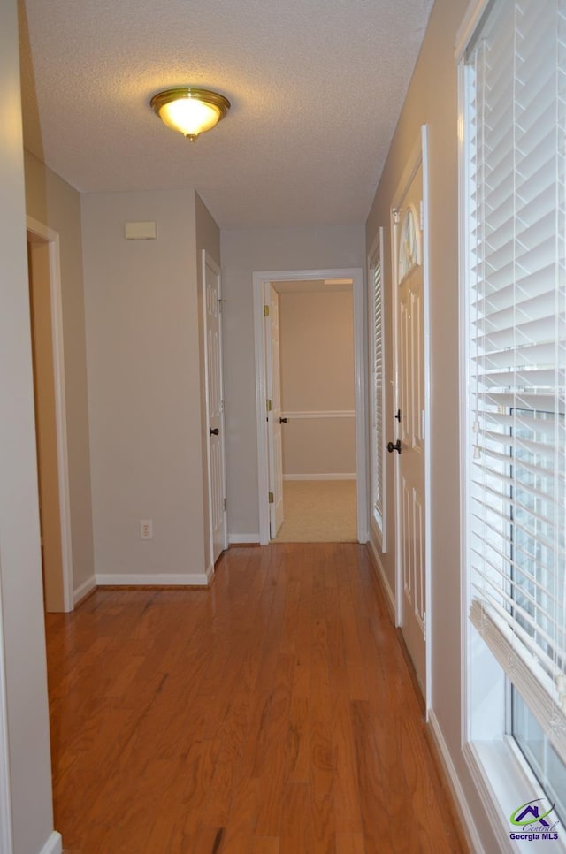 corridor with light wood-style flooring, a textured ceiling, and baseboards