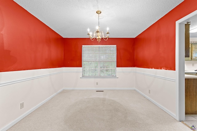 carpeted spare room with baseboards, a notable chandelier, and a textured ceiling