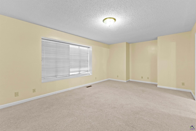 empty room featuring a textured ceiling, light colored carpet, baseboards, and visible vents
