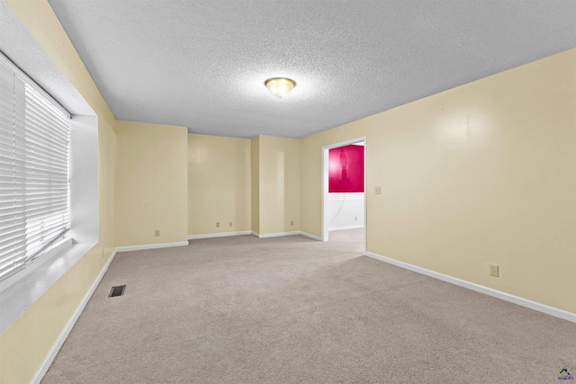 carpeted spare room featuring visible vents, baseboards, and a textured ceiling