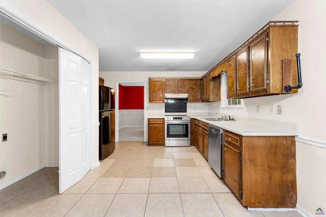 kitchen with light countertops, under cabinet range hood, brown cabinets, appliances with stainless steel finishes, and a sink
