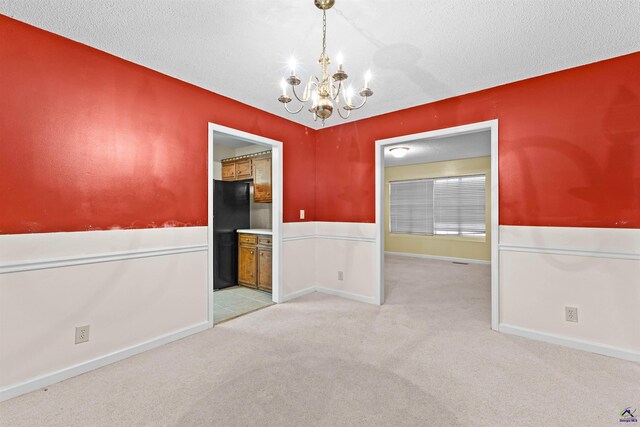 spare room featuring carpet flooring, a notable chandelier, and a textured ceiling