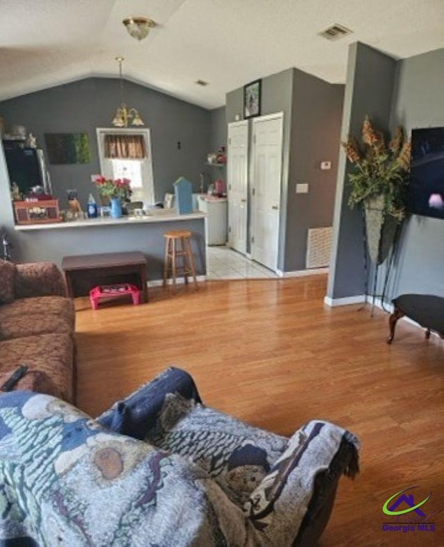 living area featuring baseboards, vaulted ceiling, visible vents, and light wood-style flooring