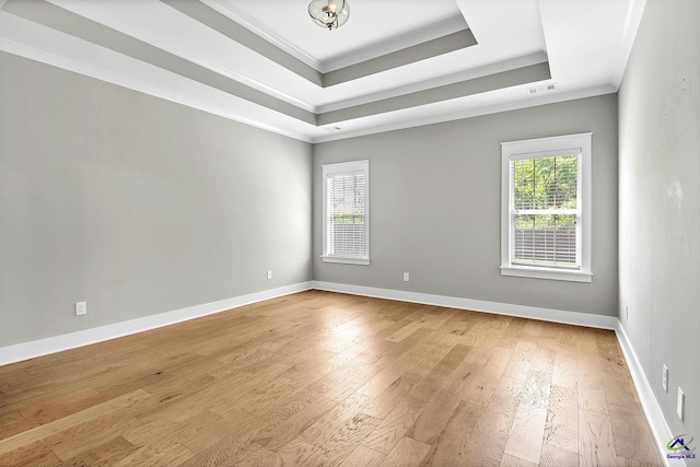 empty room featuring light wood-style floors, visible vents, a tray ceiling, and ornamental molding