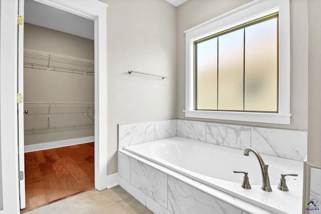 bathroom with a wealth of natural light, a walk in closet, a garden tub, and tile patterned floors