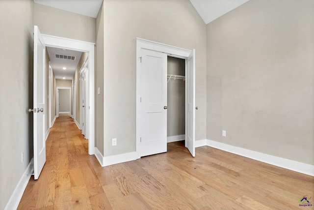 unfurnished bedroom featuring visible vents, baseboards, a closet, light wood finished floors, and vaulted ceiling