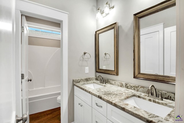 full bathroom with toilet, wood finished floors, double vanity, and a sink