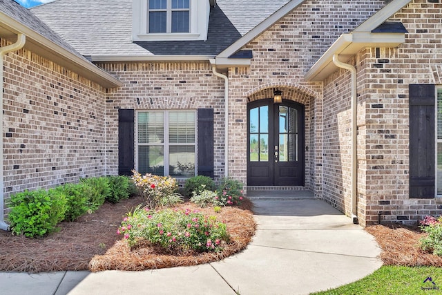doorway to property featuring brick siding, roof with shingles, and french doors