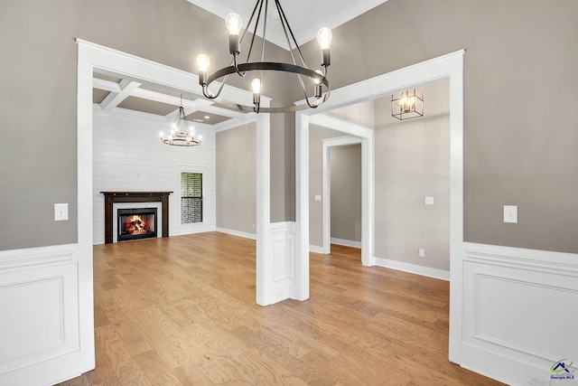 unfurnished dining area featuring coffered ceiling, light wood finished floors, a notable chandelier, and ornamental molding