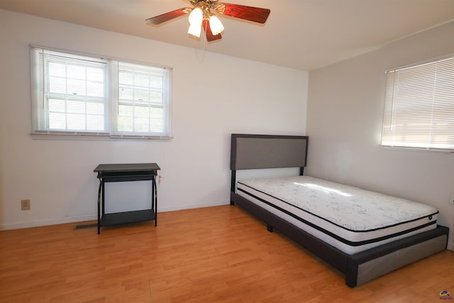 bedroom featuring light wood-style flooring, multiple windows, baseboards, and a ceiling fan
