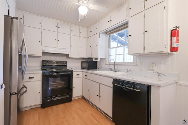 kitchen with a sink, under cabinet range hood, black appliances, light wood finished floors, and white cabinetry