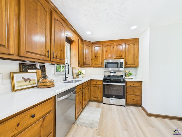 kitchen with a sink, light countertops, appliances with stainless steel finishes, light wood-style floors, and brown cabinets