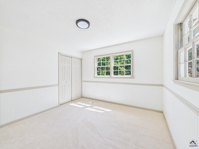 unfurnished bedroom featuring carpet floors, a closet, wainscoting, and a textured ceiling