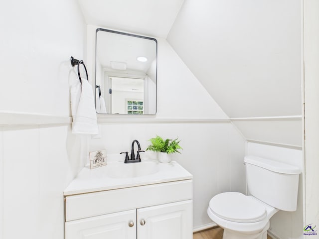 half bath with toilet, wood finished floors, and vanity