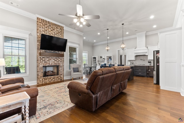 living area featuring dark wood-style flooring, ceiling fan, a fireplace, crown molding, and recessed lighting