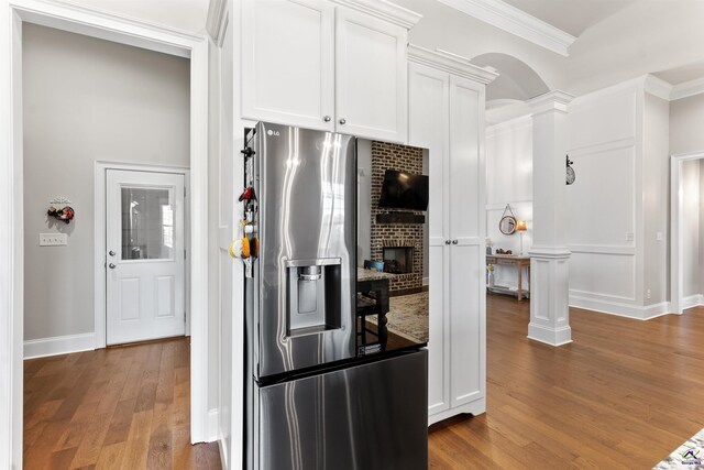 kitchen with arched walkways, stainless steel refrigerator with ice dispenser, ornamental molding, decorative columns, and wood finished floors