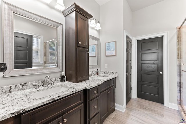 bathroom with double vanity, a tile shower, baseboards, and a sink