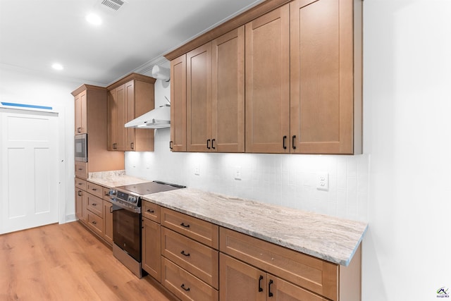 kitchen with stainless steel appliances, light wood finished floors, backsplash, wall chimney exhaust hood, and light stone countertops