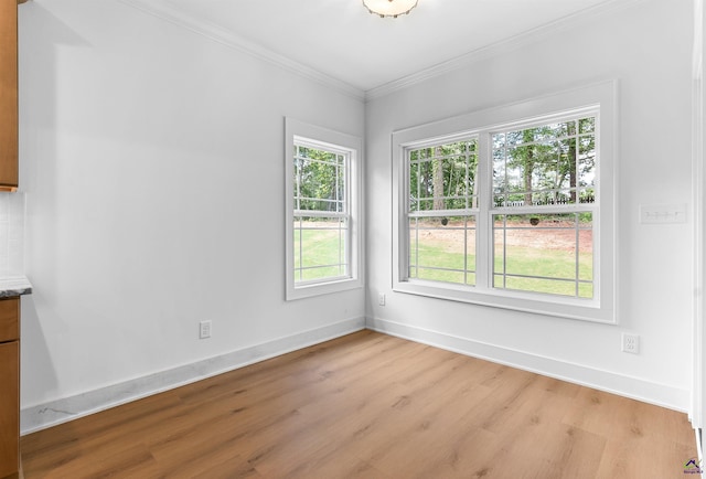 empty room with crown molding, light wood-type flooring, and baseboards