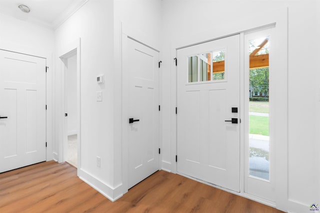 entryway with light wood-type flooring, crown molding, and baseboards