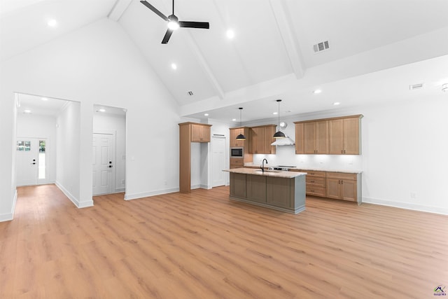 kitchen featuring high vaulted ceiling, ceiling fan, stainless steel microwave, a center island with sink, and light wood-style flooring
