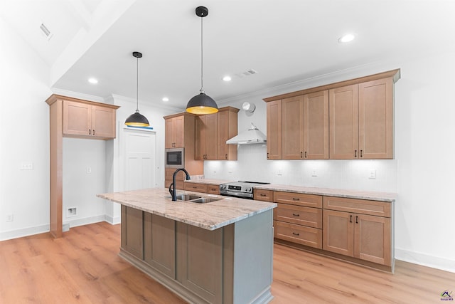 kitchen featuring a sink, stainless steel appliances, light stone counters, light wood-style floors, and an island with sink