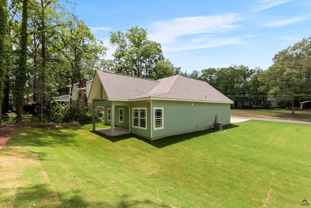 view of side of home with a lawn, central AC, a patio, a shingled roof, and view of scattered trees