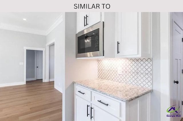 104 Reedy Ct, Perry, GA 31069 - kitchen with stainless steel microwave, crown molding, light wood-type flooring, white cabinetry, and decorative backsplash