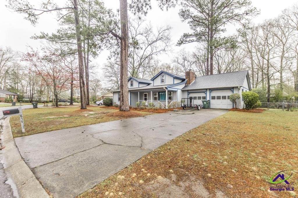 view of front facade with a garage, concrete driveway, a chimney, covered porch, and a front yard