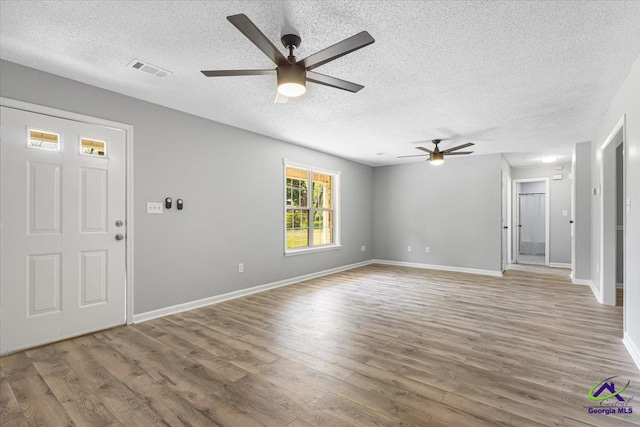 unfurnished living room featuring a textured ceiling, ceiling fan, light wood finished floors, baseboards, and visible vents