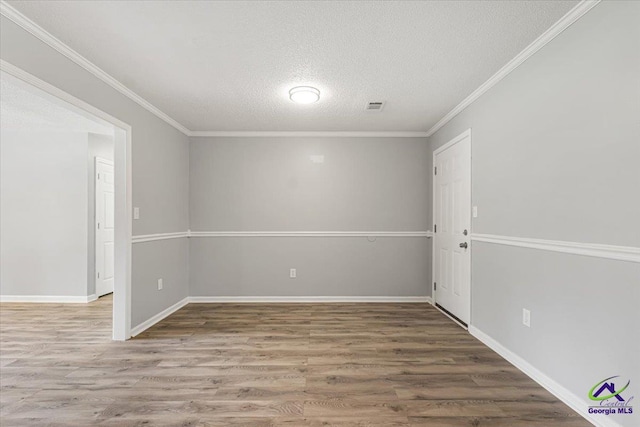 empty room featuring wood finished floors, a textured ceiling, baseboards, ornamental molding, and visible vents