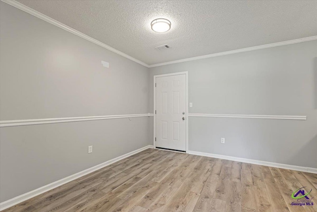 spare room with a textured ceiling, wood finished floors, visible vents, and ornamental molding