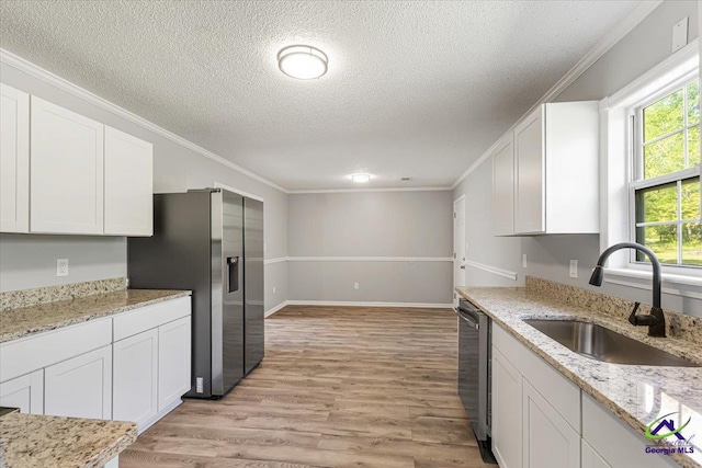 kitchen featuring white cabinets, stainless steel appliances, ornamental molding, a sink, and a textured ceiling
