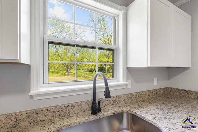 details with white cabinets, light stone countertops, and a sink
