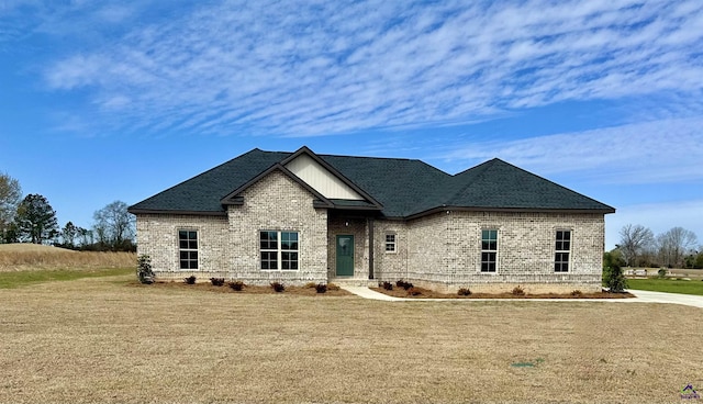 view of front of property with a shingled roof, a front lawn, and brick siding