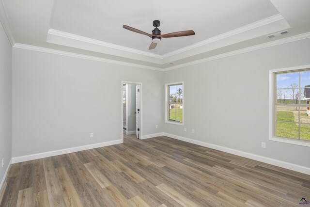 empty room featuring a raised ceiling, wood finished floors, visible vents, a ceiling fan, and baseboards