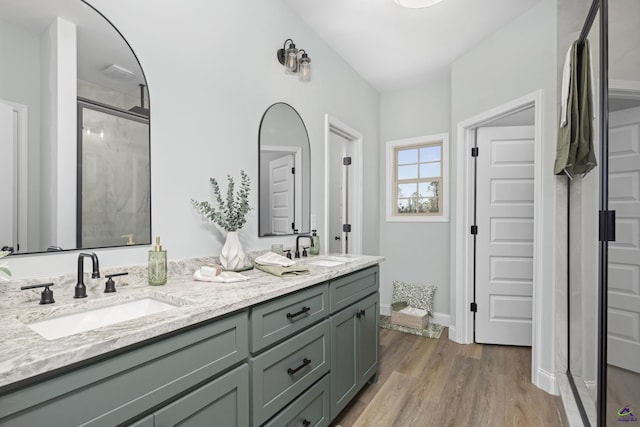 full bath with double vanity, a stall shower, wood finished floors, and a sink