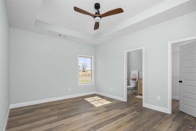 unfurnished bedroom featuring visible vents, baseboards, a raised ceiling, a walk in closet, and wood finished floors